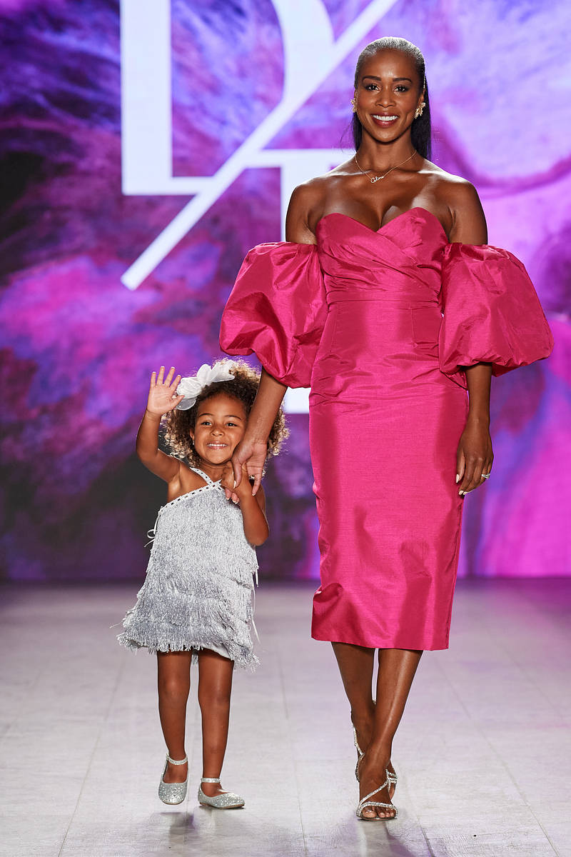 A little girl in a silver tassled dress walking down the runway with her mum, who is wearing a satin pink dress